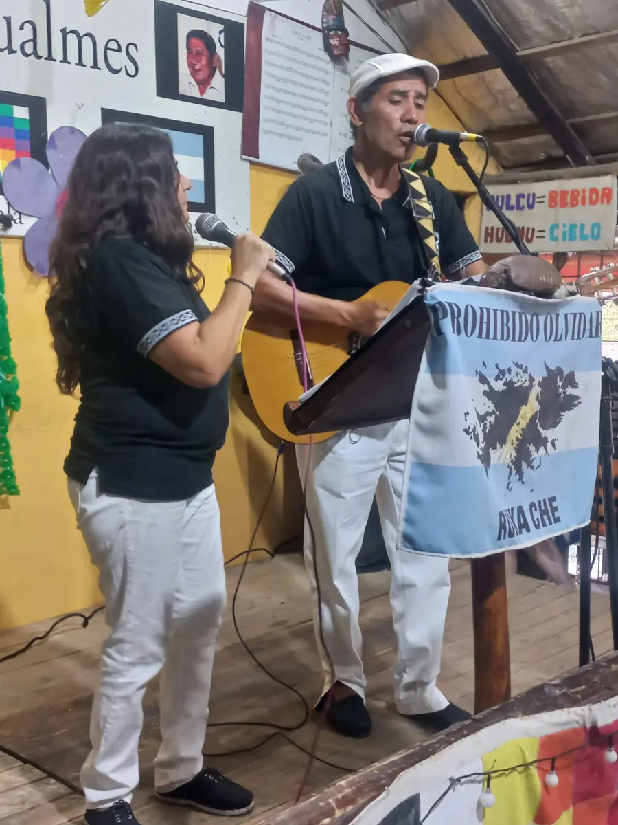 Lina y Eduardo cantando en el Escenario Remigio Gualmes junto a la bandera de Malvinas