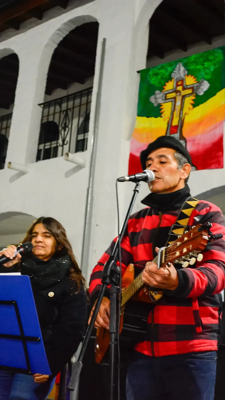 Eduardo tocando guitarra criolla y cantando con boina y campera a rayas rojas y negras