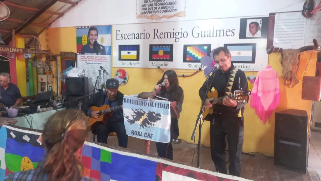 Grupo folklórico en vivo con banderas de pueblos originarios de fondo